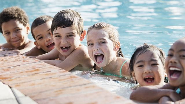 Group of children at edge of pool smiling widely